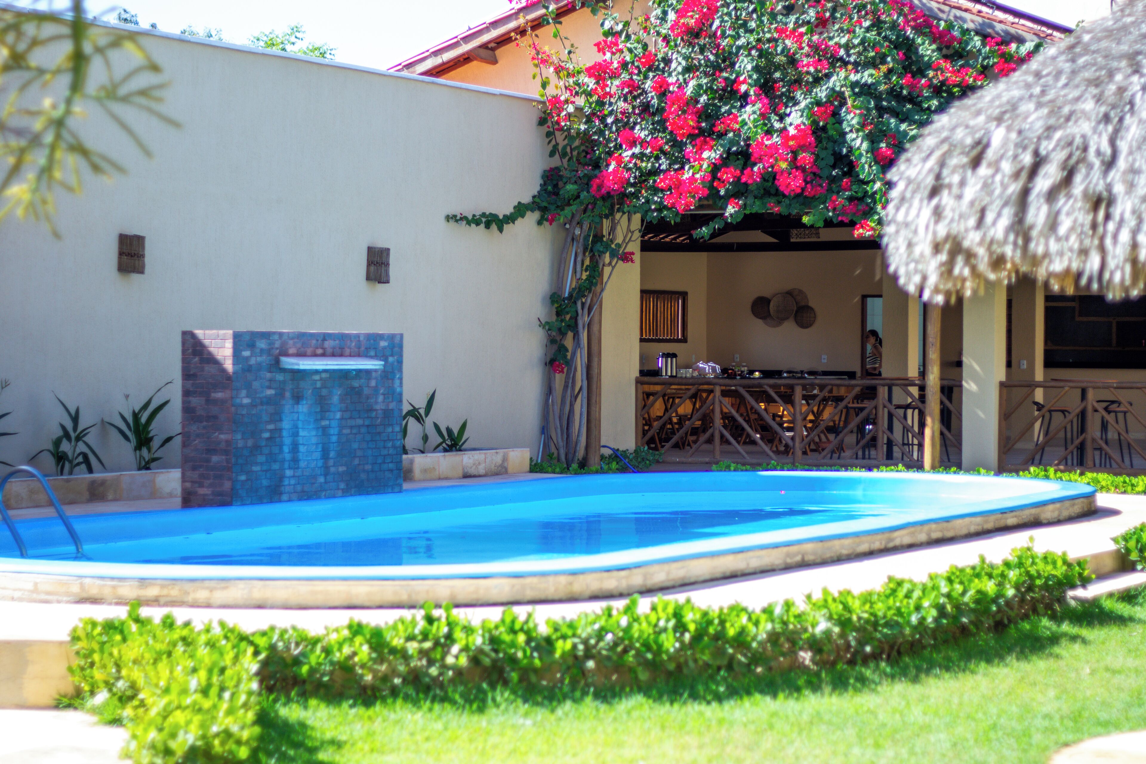 A swimming pool with a stone structure, surrounded by greenery and a building with a thatched roof.