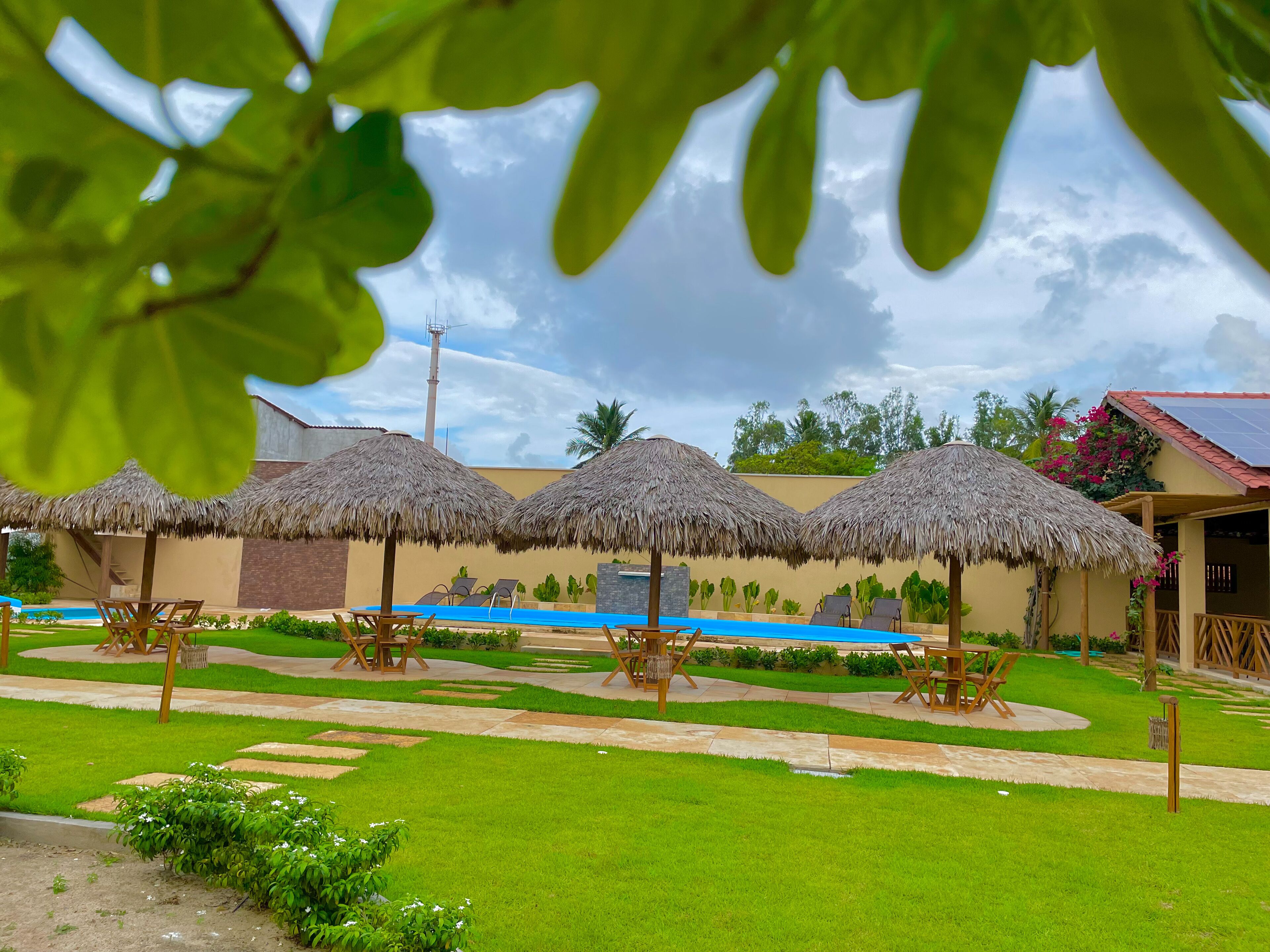Ein Resort mit Pool, Reetdachschirmen und einem gepflegten Rasen.