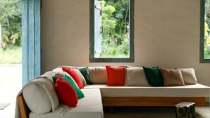 Una habitación con un banco de madera, una mesita y un ventanal con vistas a zonas verdes.