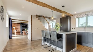 Een moderne keuken met een centraal eiland, barstoelen en een trap naar een vide met woonruimte.