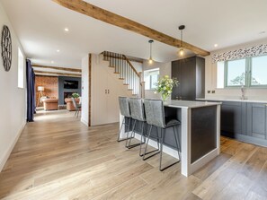 Een moderne keuken met een centraal eiland, barstoelen en een trap naar een vide met woonruimte.