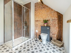 A bathroom with a glass-enclosed shower, a toilet, and a brick wall.