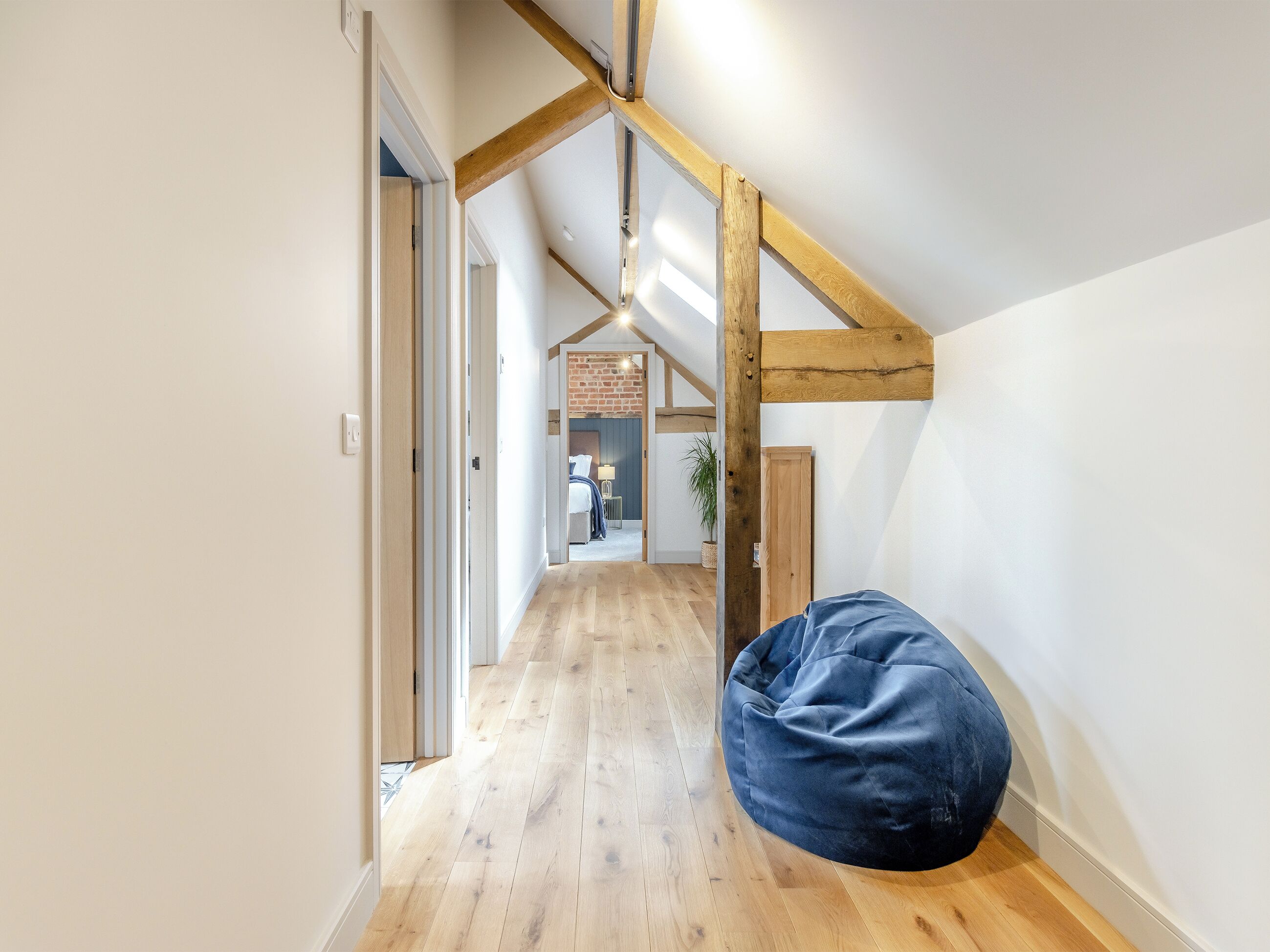 Un pasillo con vigas de madera, un sillón de pelota azul y una cama a lo lejos.
