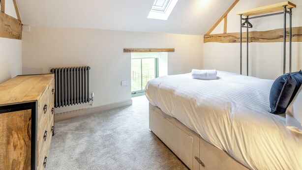 Een slaapkamer met een bed, een radiator, een houten dressoir, een dakraam en een raam.