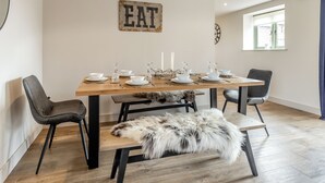 Een eethoek met een houten tafel voor vier personen, zwarte stoelen, een bont plaid en een bord waarop 'EAT' staat.