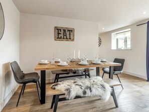 A dining area with a wooden table set for four, black chairs, a fur throw, and a wall sign that reads 'EAT'.
