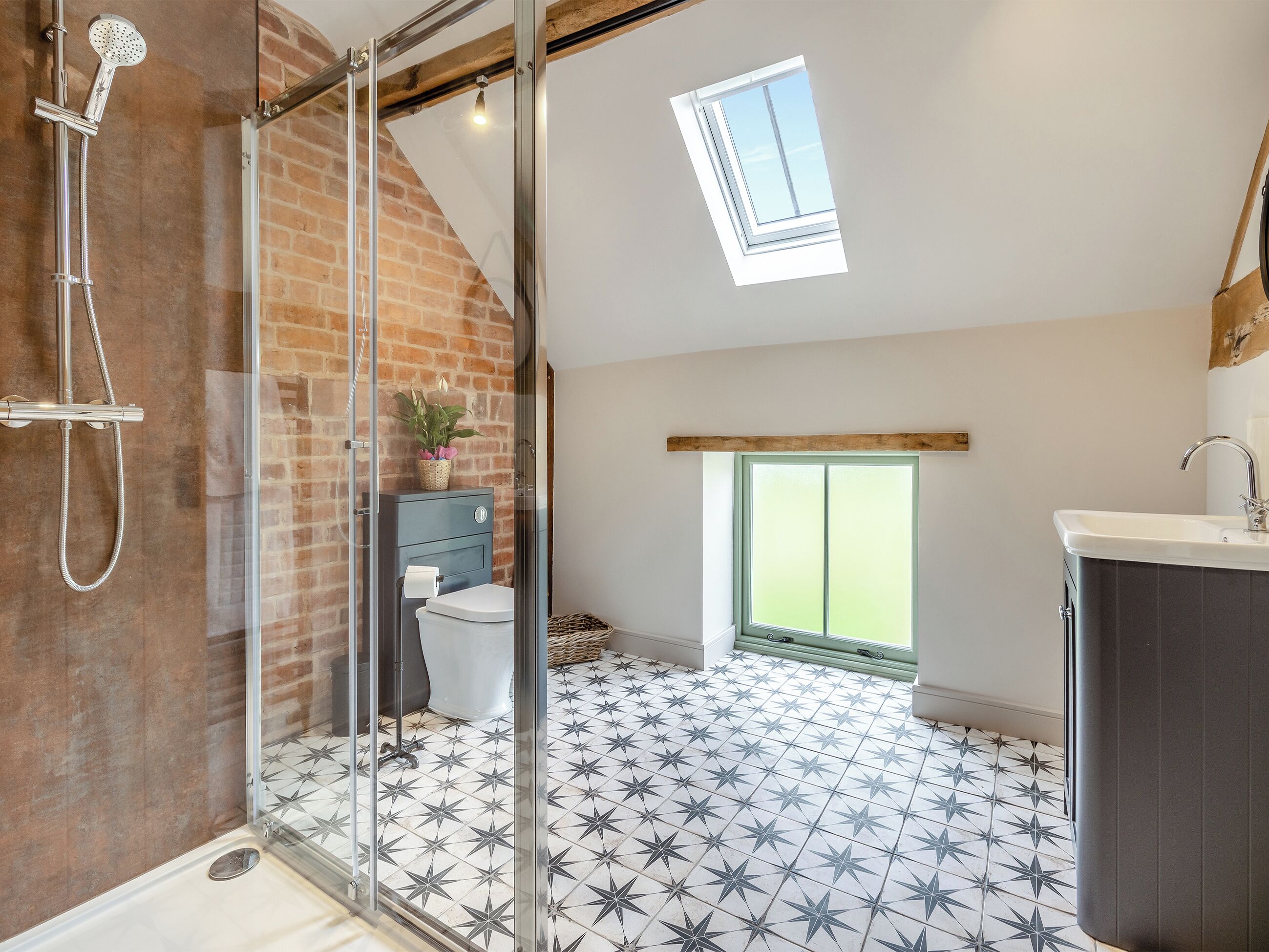 Un baño moderno con ducha, inodoro y lavamanos, que cuenta con un suelo estampado con motivos de estrellas y un tragaluz.