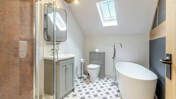 A bathroom with a freestanding bathtub, a glass shower enclosure, a toilet, and a skylight.