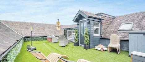 A backyard with artificial grass, two wicker chairs, a small shed, and a chimney.