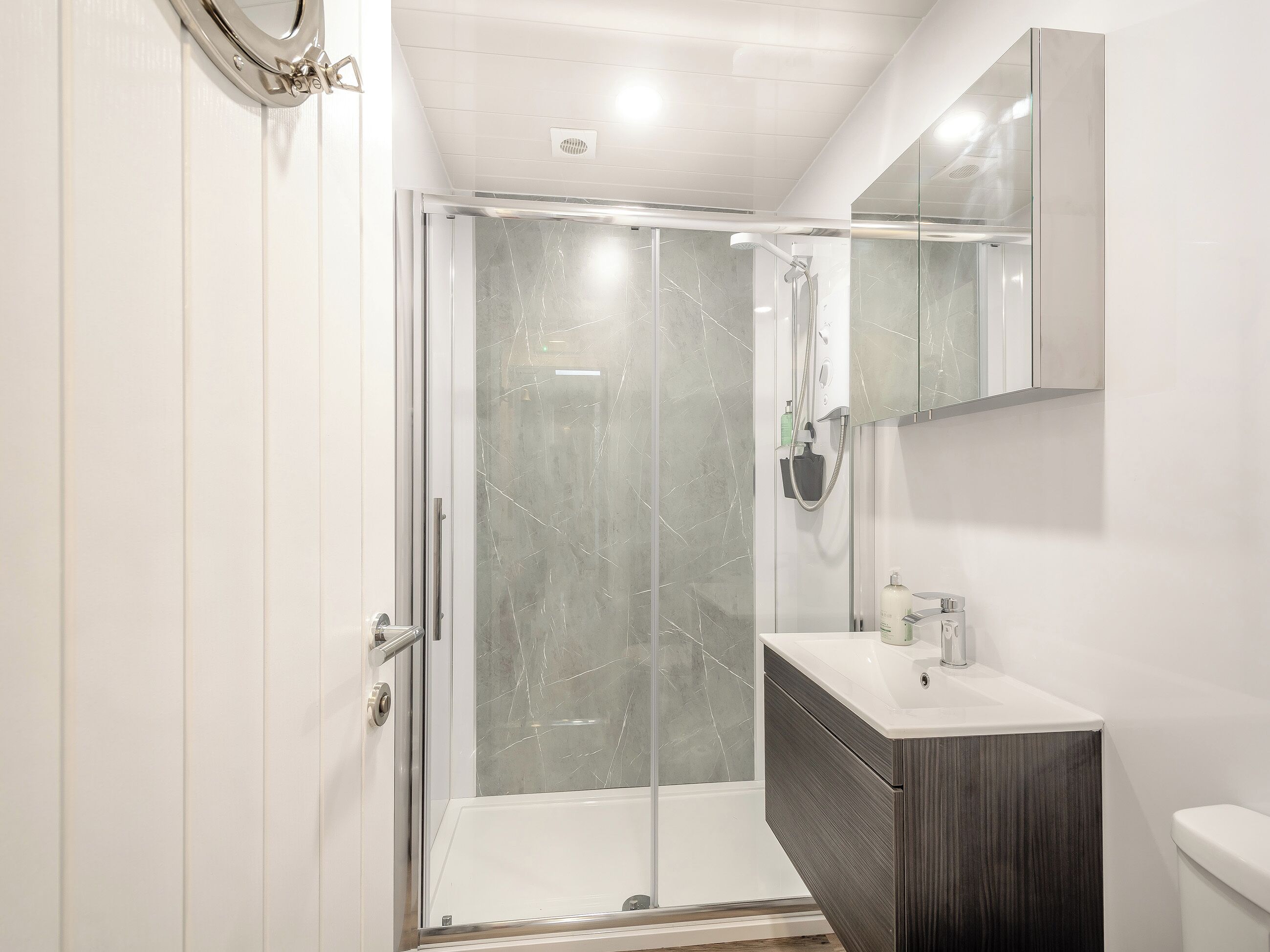 A modern bathroom with a glass-enclosed shower, a dark wood vanity, and a white toilet.