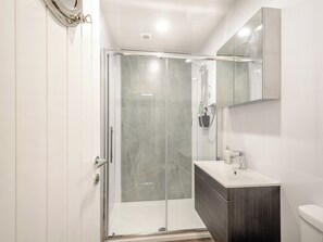 Un baño moderno con ducha de vidrio, tocador de madera oscura y un inodoro blanco.
