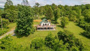 A large house with a green roof and a covered porch, surrounded by lush green trees and a well-maintained lawn. - Overlook Loft - Scenic Shenandoah Views (Elkton)