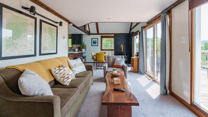 A spacious living room with a wooden coffee table, a sofa, and a dining area with chairs. - Overlook Loft - Scenic Shenandoah Views (Elkton)
