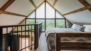 A bedroom with a large window, wooden beams, a bed, and a view of the outdoors. - Overlook Loft - Scenic Shenandoah Views (Elkton)