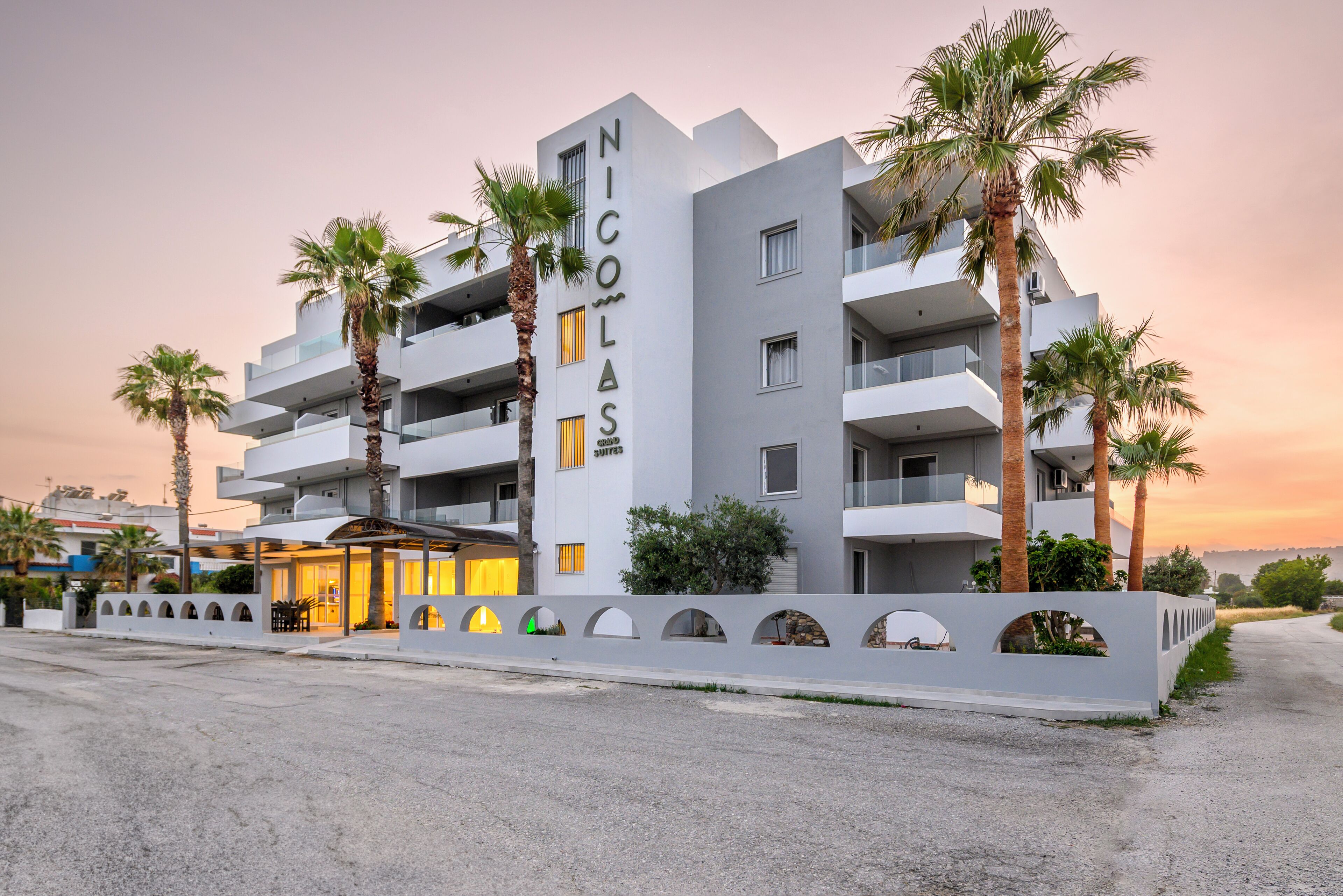 A modern hotel with a prominent name sign, multiple balconies, and palm trees.