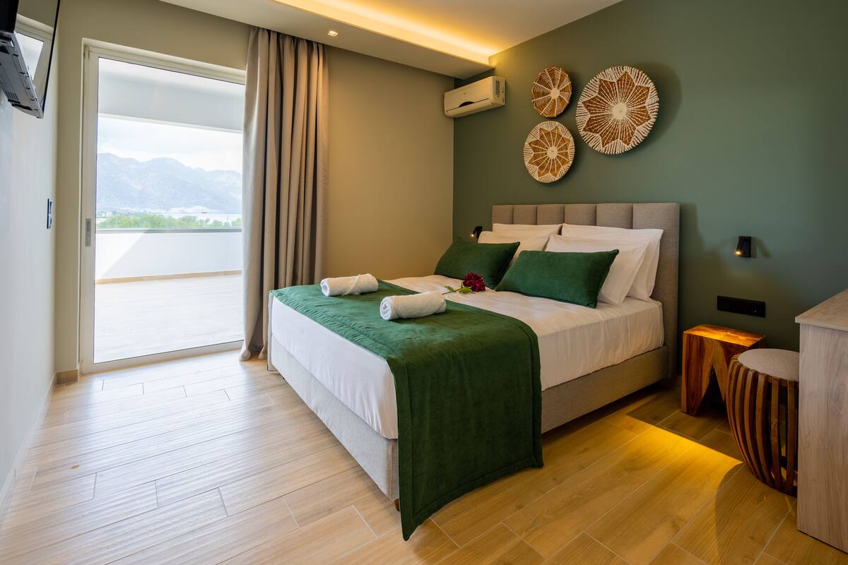 A modern hotel room with a large bed, a view of the mountains, and a balcony.