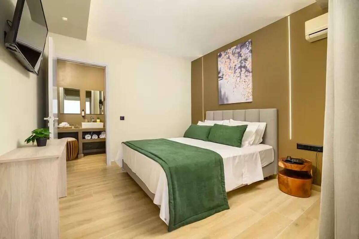A modern bedroom with a bed, a bedside table, a mirror, and a wall-mounted TV.