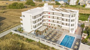 A modern hotel with multiple floors, a rooftop pool, and a view of the sea. - Nicolas Grand Suites - Adults Only (Kos)