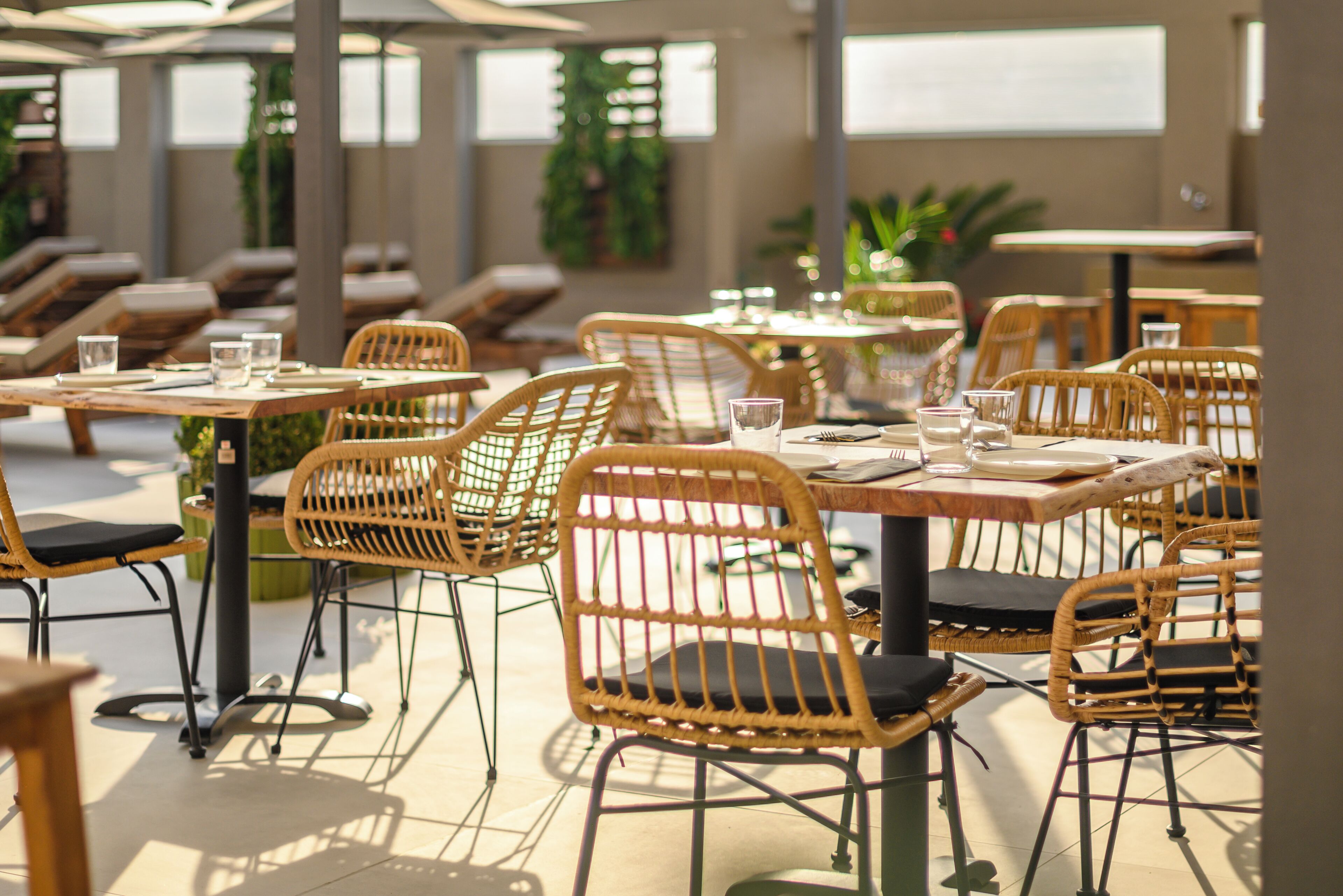 Un área de comedor al aire libre con sillas y mesas de mimbre, algunas con cojines.