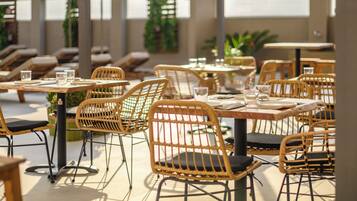 Un área de comedor al aire libre con sillas y mesas de mimbre, algunas con cojines.