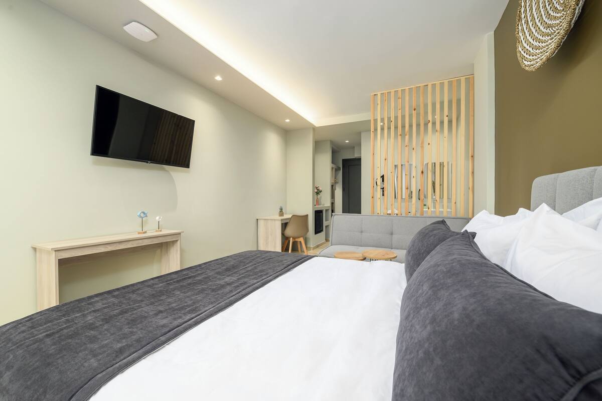 A modern hotel room with a large bed, a desk, a television, and a wooden partition.
