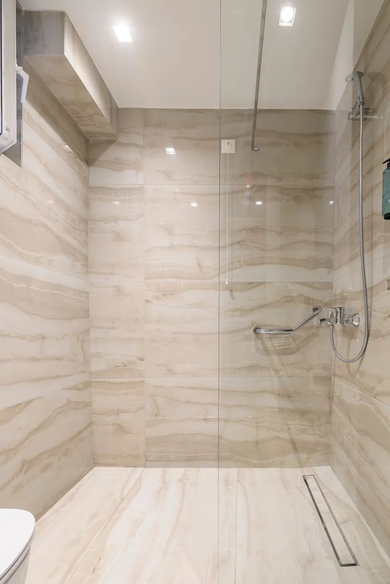A modern bathroom with a glass-enclosed shower, marble walls, and a toilet.