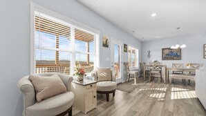 Un amplio salón con sofá, mesa de comedor y sillas, ventanas grandes con persianas y vistas al exterior.