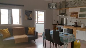 Sala de estar con sofá, mesa de comedor, sillas y una zona de cocina con estufa, microondas y armarios.