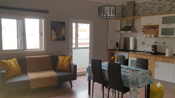 A living room with a sofa, dining table, chairs, and a kitchen area with a stove, microwave, and cabinets.