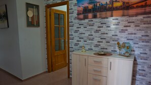 Un pasillo con una puerta de madera, un armario color crema con cajones y una pared de ladrillo decorada con una pintura de paisaje urbano.