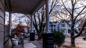 A covered porch with benches, a stone pillar, and a view of residential houses.