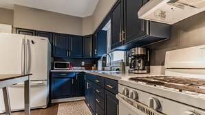 A modern kitchen with dark blue cabinets, a white refrigerator, a microwave, a gas stove, and a coffee maker.