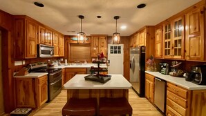 Una cocina con armarios de madera, una isla central con asientos, electrodomésticos de acero inoxidable e iluminación colgante.
