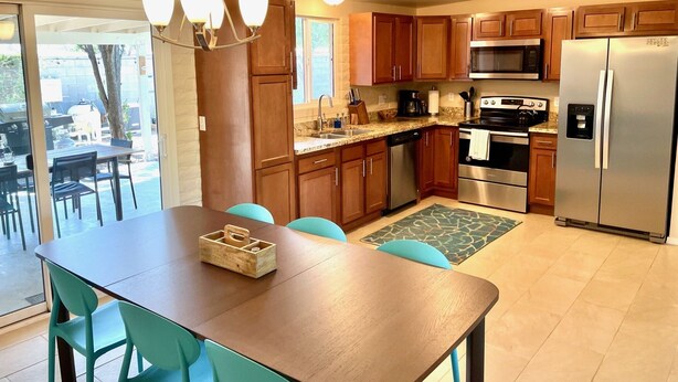 A modern kitchen with wooden cabinets, stainless steel appliances, and a dining area with a wooden table and turquoise chairs. - Desert Oasis w/Pool & Spa Close to Saguaro National Park (Tucson)