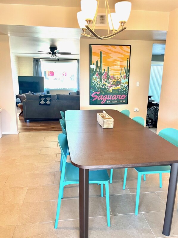 Un coin repas avec une table en bois et des chaises turquoise, un canapé en arrière-plan et une affiche du parc national de Saguaro.