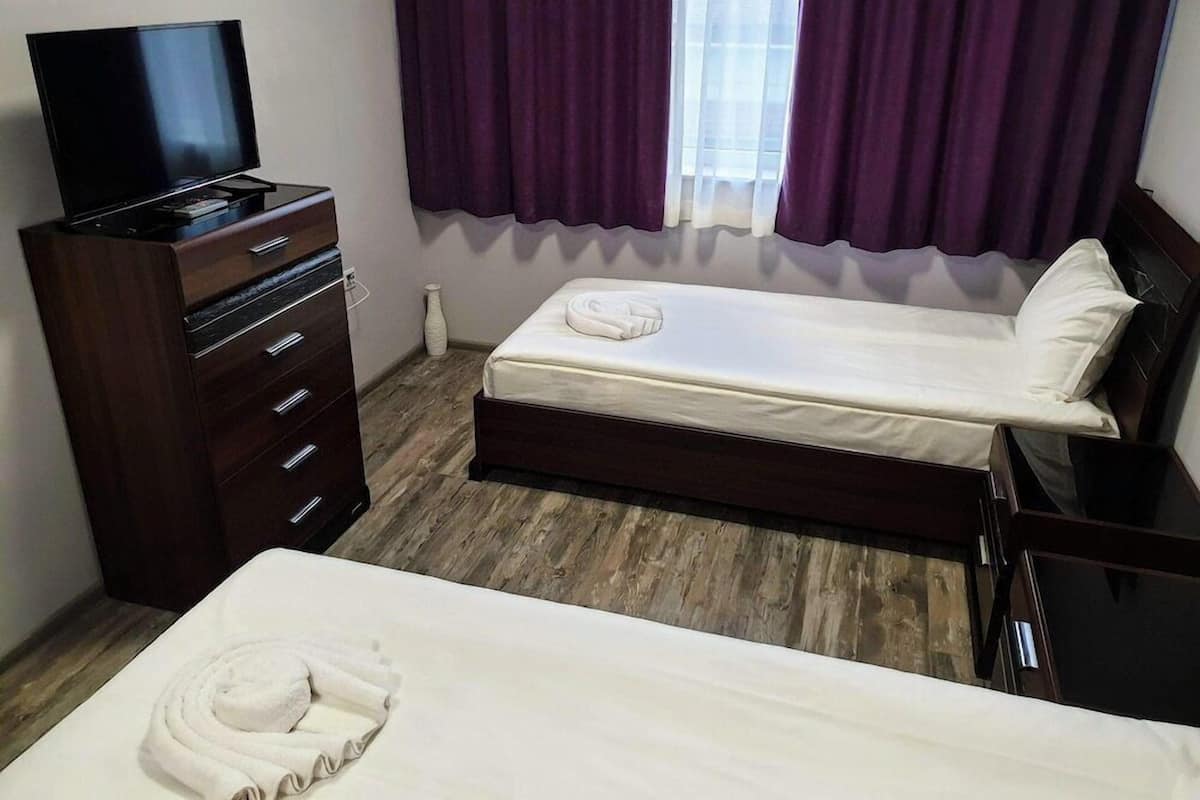 A hotel room with a bed, a TV on a dresser, and a window with curtains.