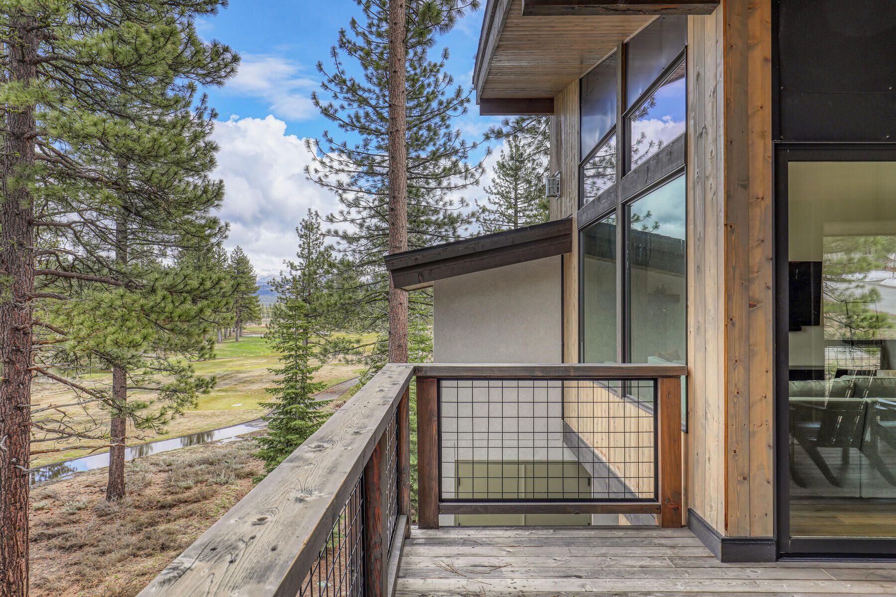 A modern building with large windows, a wooden deck, and a view of a forested area.