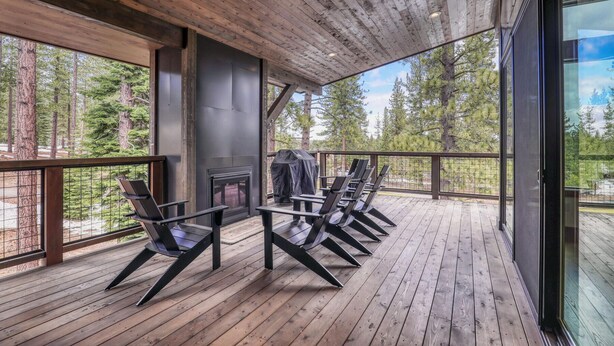 Una terraza de madera con chimenea, asientos al aire libre y vistas al bosque.