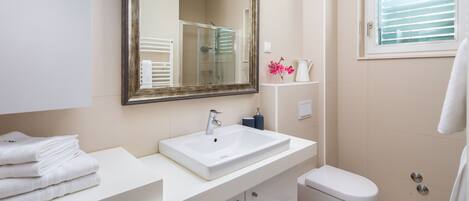 A bathroom with a white sink, a mirror, a toilet, and a shower.