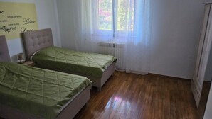 Een slaapkamer met twee bedden, een radiator en een raam met dunne gordijnen.
