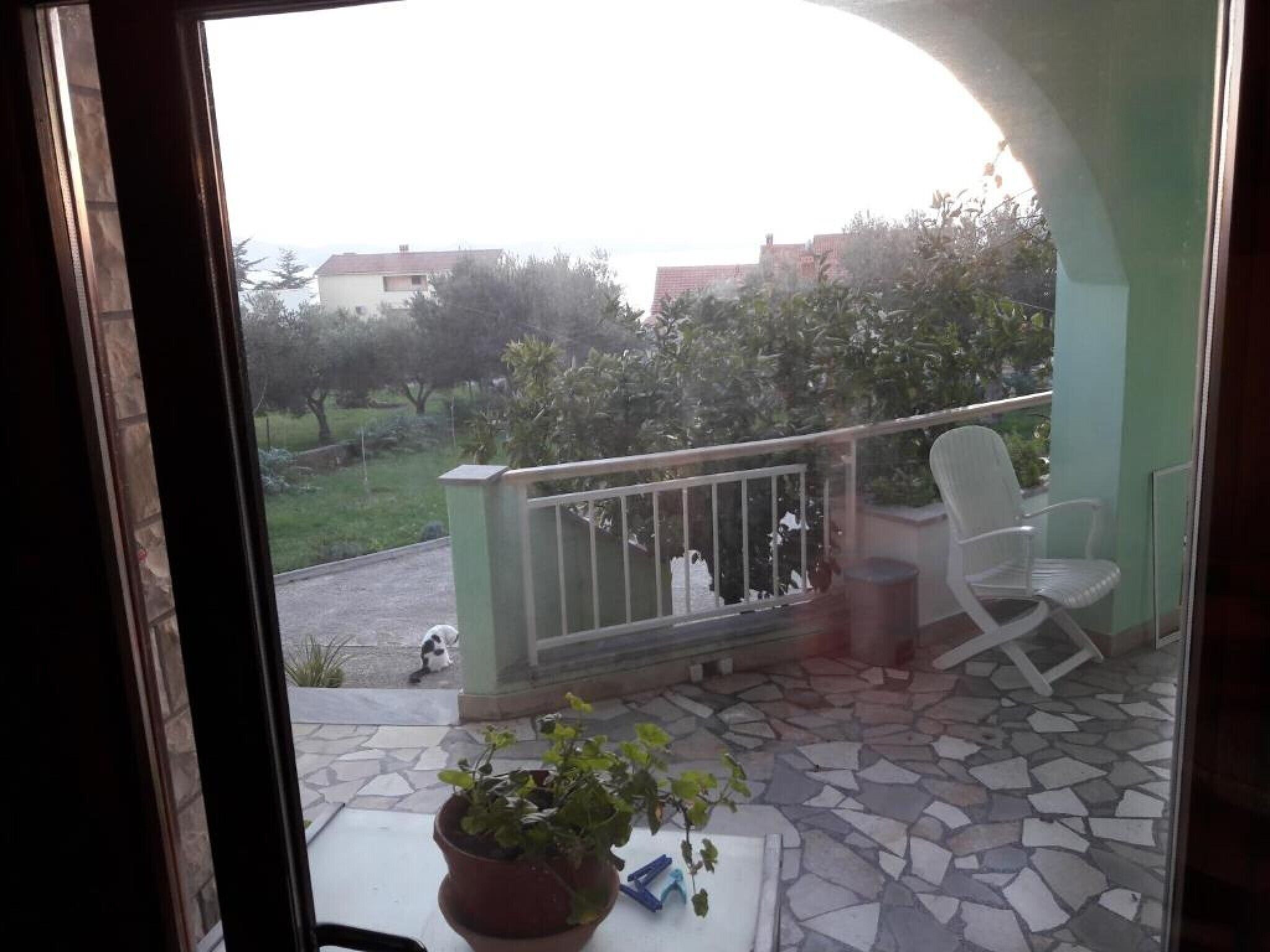 Een balkon met een bloempot, een witte stoel en een betegelde vloer.