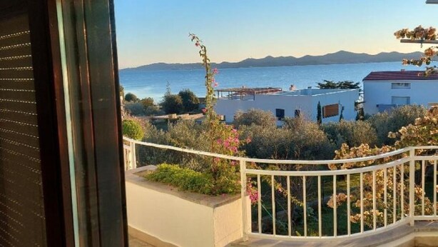 Un balcon offrant une vue sur la mer et les montagnes, un sol en pierre et une balustrade blanche.
