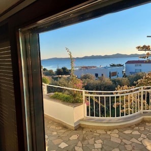 Un balcon offrant une vue sur la mer et les montagnes, un sol en pierre et une balustrade blanche.