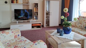 A living room with a flat-screen TV, a bookshelf, a wardrobe, and a floral sofa. - Haus Lieberum, Gemütliche Ferienwohnung Direkt am Kurpark (Bad Sooden-Allendorf)