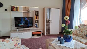 Ein Wohnzimmer mit Flachbildfernseher, Bücherregal, Kleiderschrank und einem blumigen Sofa.