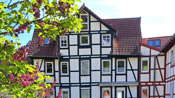 A traditional half-timbered house with a red umbrella, two lounge chairs, and well-manicured garden. - Haus Lieberum, Gemütliche Ferienwohnung Direkt am Kurpark (Bad Sooden-Allendorf)