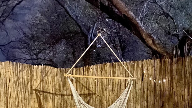Eine Hängematte, die an einer Holzkonstruktion im Freien befestigt ist, mit einer Bambuswand und Felsen im Hintergrund.