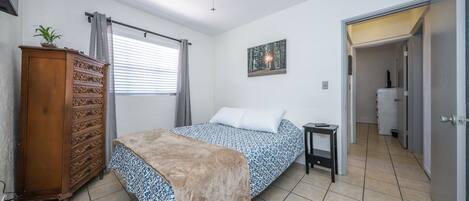 Une chambre à coucher avec un lit, une commode, un ventilateur de plafond et un tableau accroché au mur.