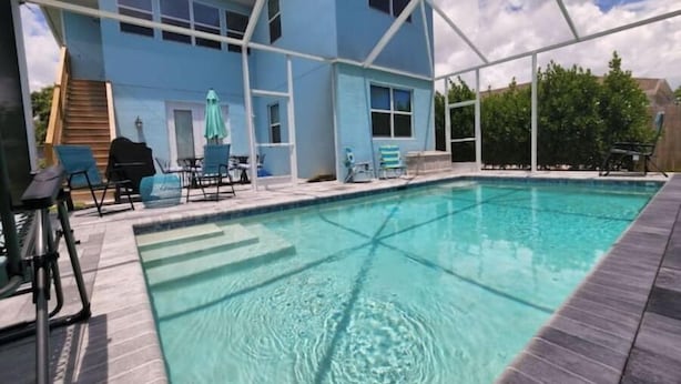 En swimmingpool med en overdækket terrasse, en blå bygning og udendørs møbler.