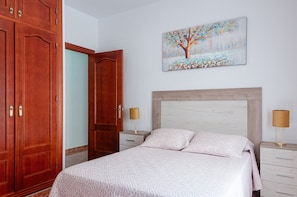 Een slaapkamer met een bed, nachtkastje, lamp, kast en een schilderij aan de muur.